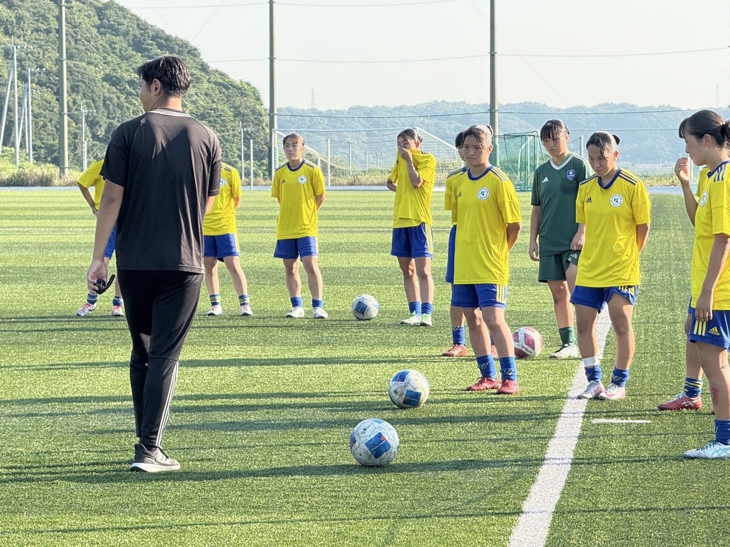 人工芝グラウンドでスタッフの説明を聞く女子サッカー部の選手